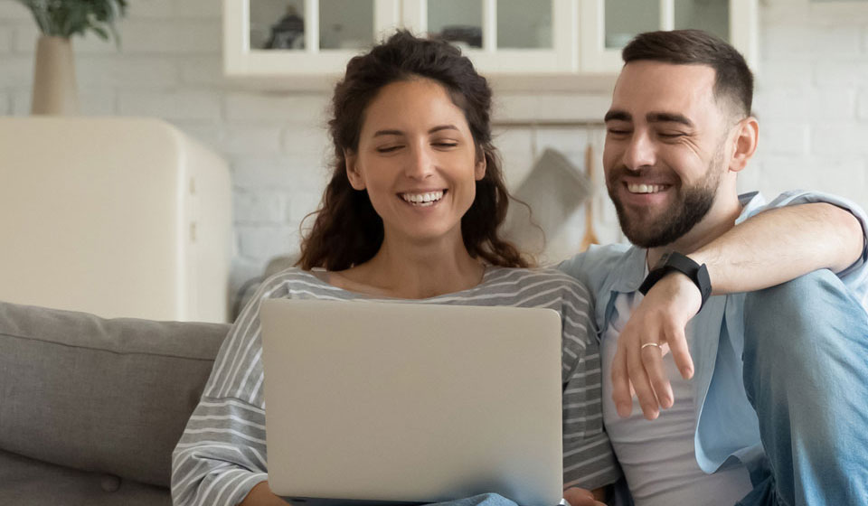 Happy couple sitting on a comfy sofa using their laptop